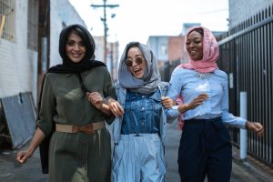 joyful multiethnic women in headscarves walking on street