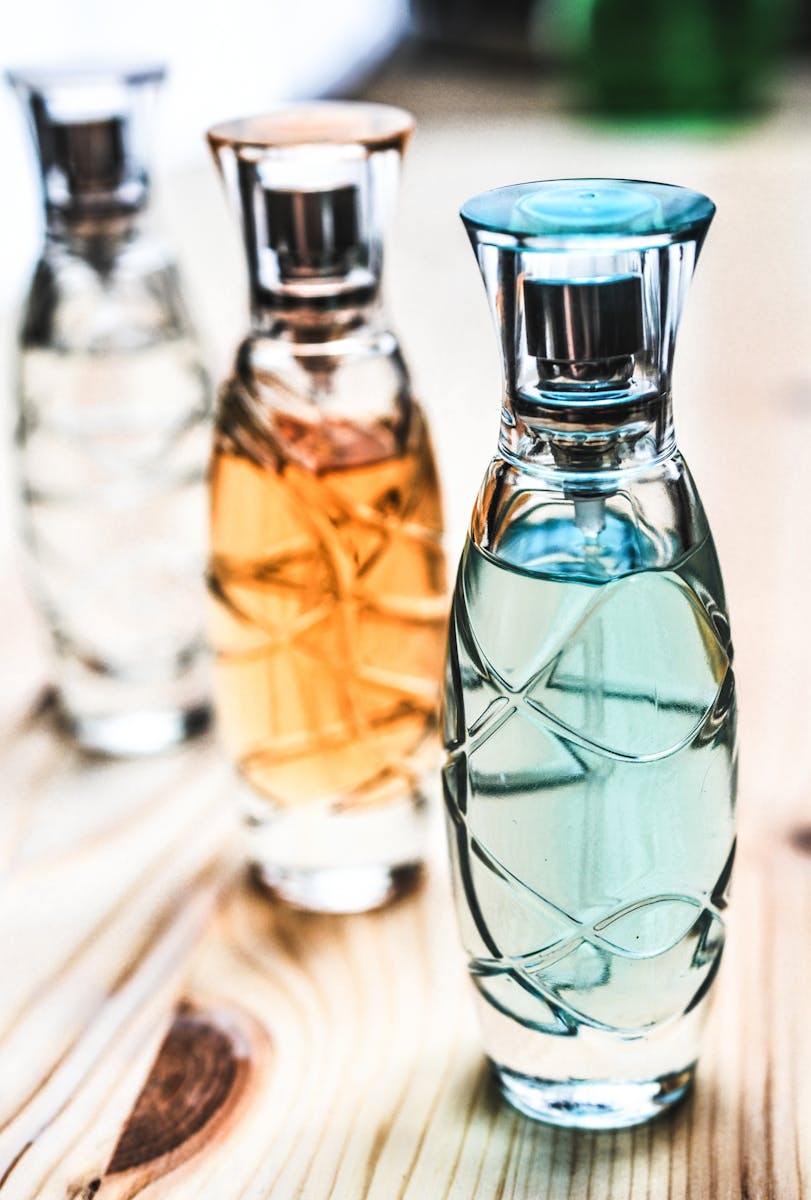 Three Assorted Clear Glass Perfume Spray Bottles on Brown Wooden Surface