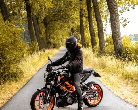 man riding black and orange motorcycle beside trees