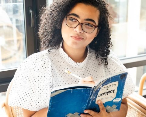 woman in white and black polka dot shirt holding blue and white book